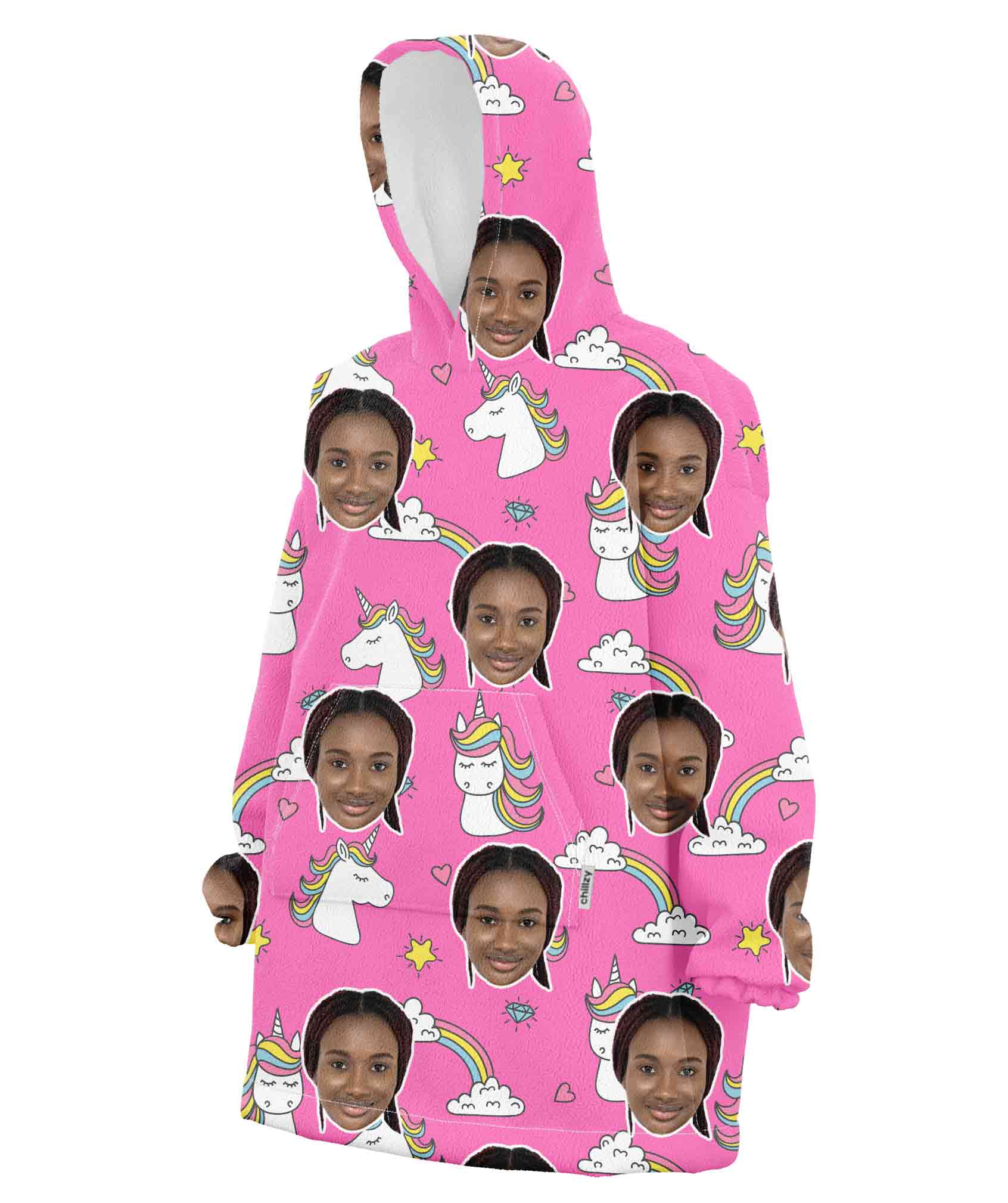 A pink hooded blanket with a pattern of a person's face and cartoonish unicorns and rainbows.
