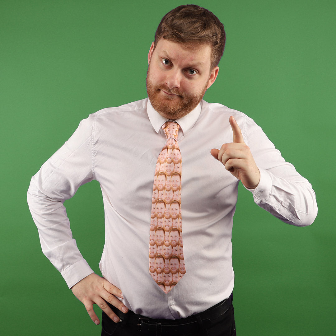 A person wearing a white shirt and a tie with a pattern of faces. The background is green.